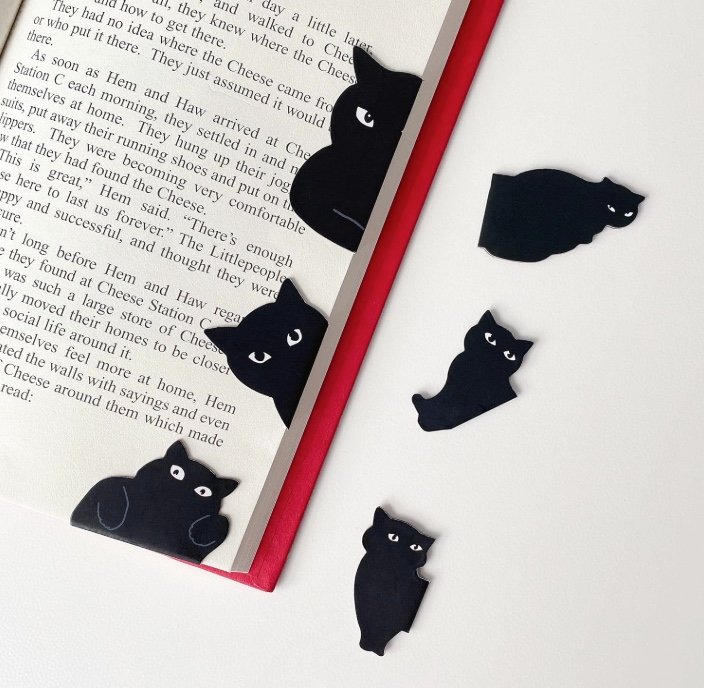 Black cat-shaped magnetic bookmarks clipped to an open book and displayed on a white surface.